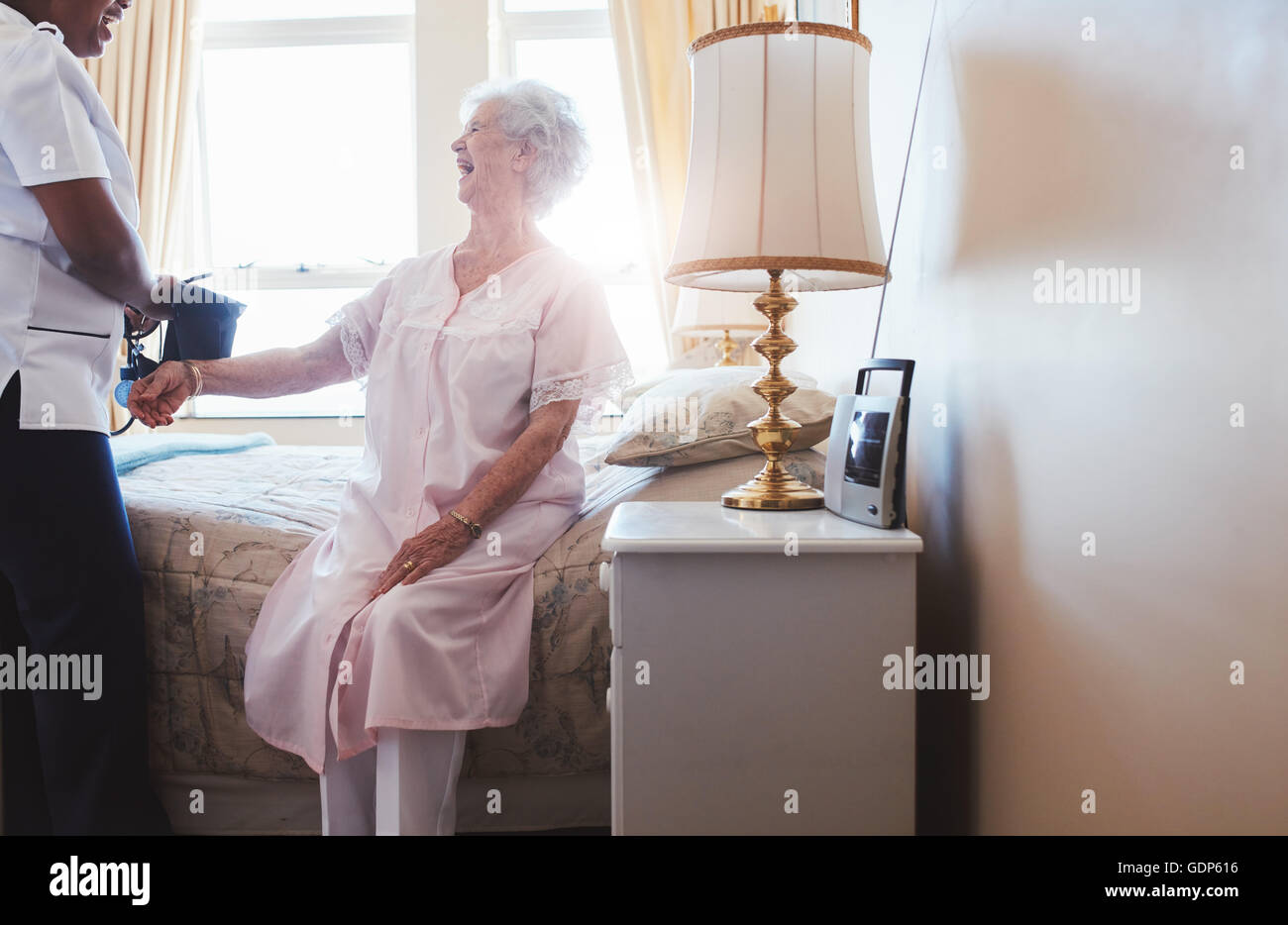 Tourné à l'intérieur d'happy senior woman sitting on bed with female nurse contrôler la pression artérielle. Aide familiale dépistage pressu Banque D'Images