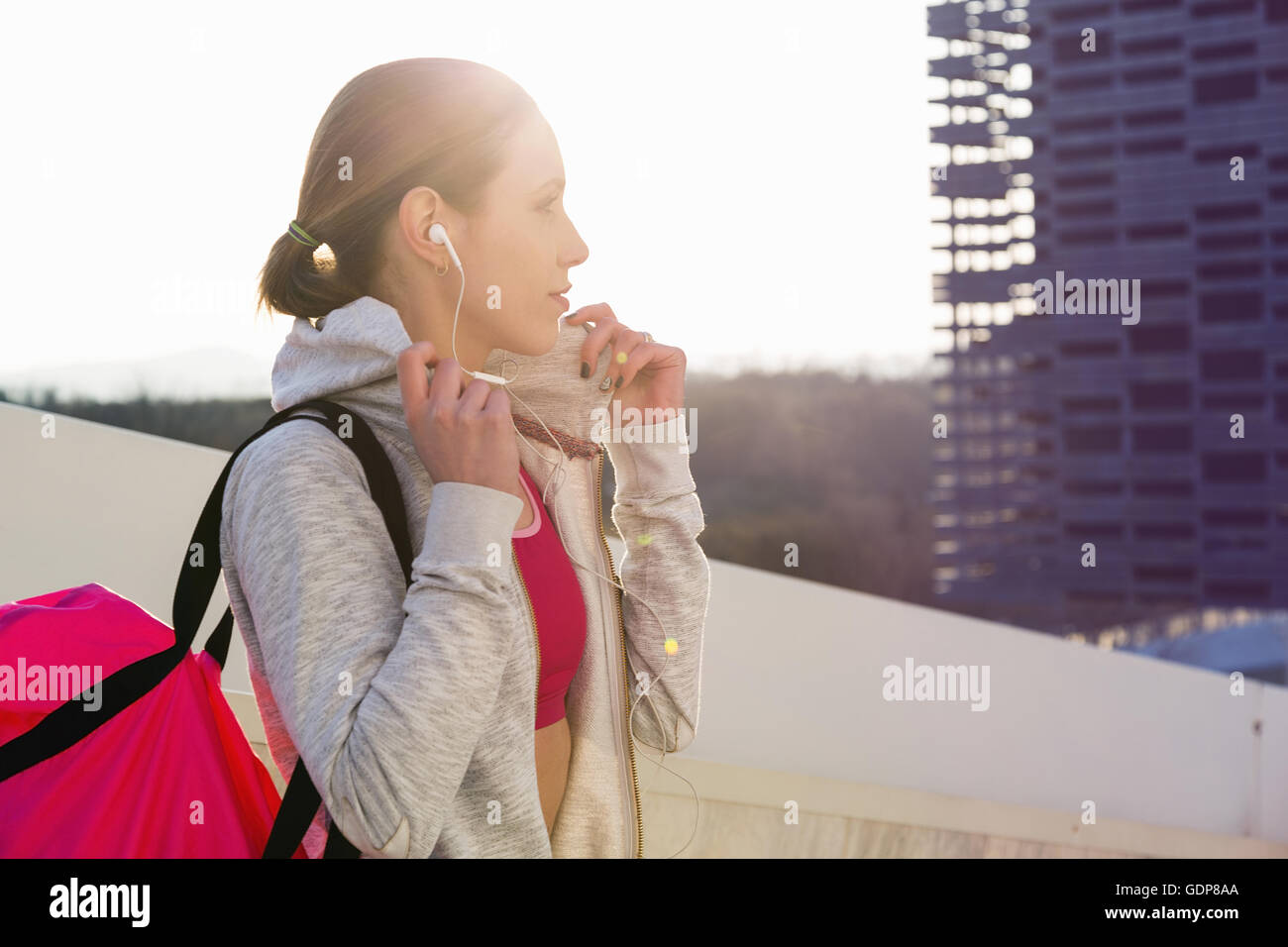 Jeune femme à l'extérieur, le port de vêtements de sport et d'écouteurs, transportant un sac de sport Banque D'Images