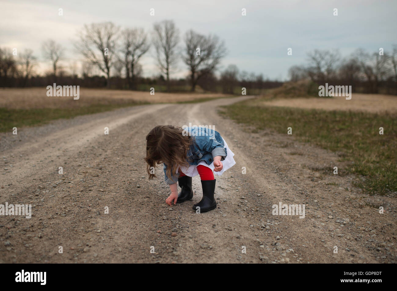 Young Girl picking up pierre de chemin de terre Banque D'Images