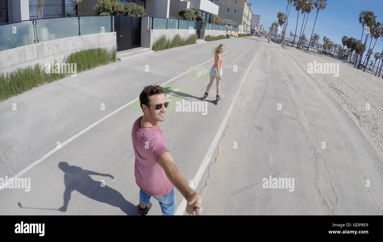 Vue arrière du patin à roues alignées en couple, selfies Venice Beach, Californie, USA Banque D'Images
