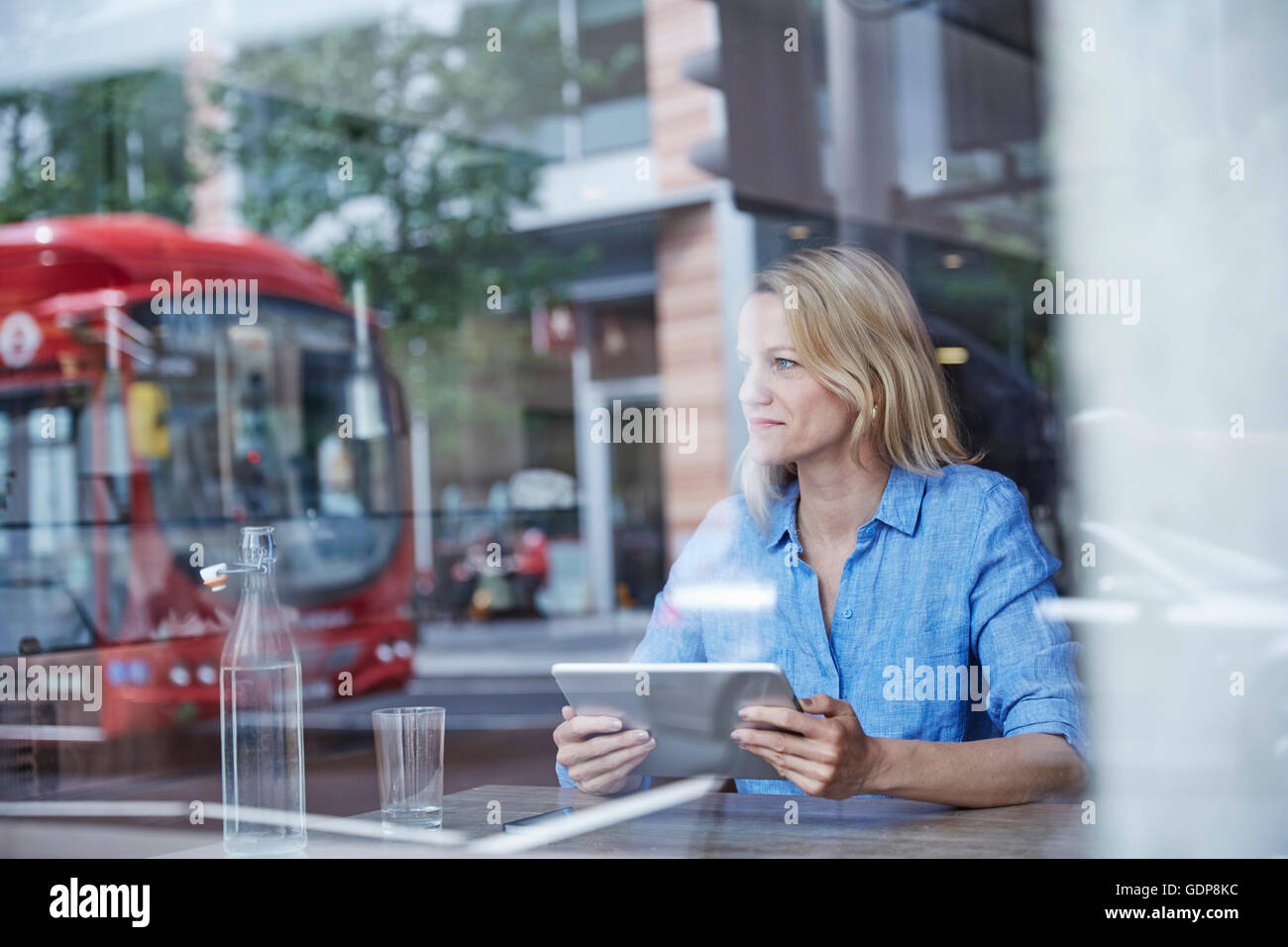 Mature Woman sitting in cafe, using digital tablet, bus reflète dans window Banque D'Images
