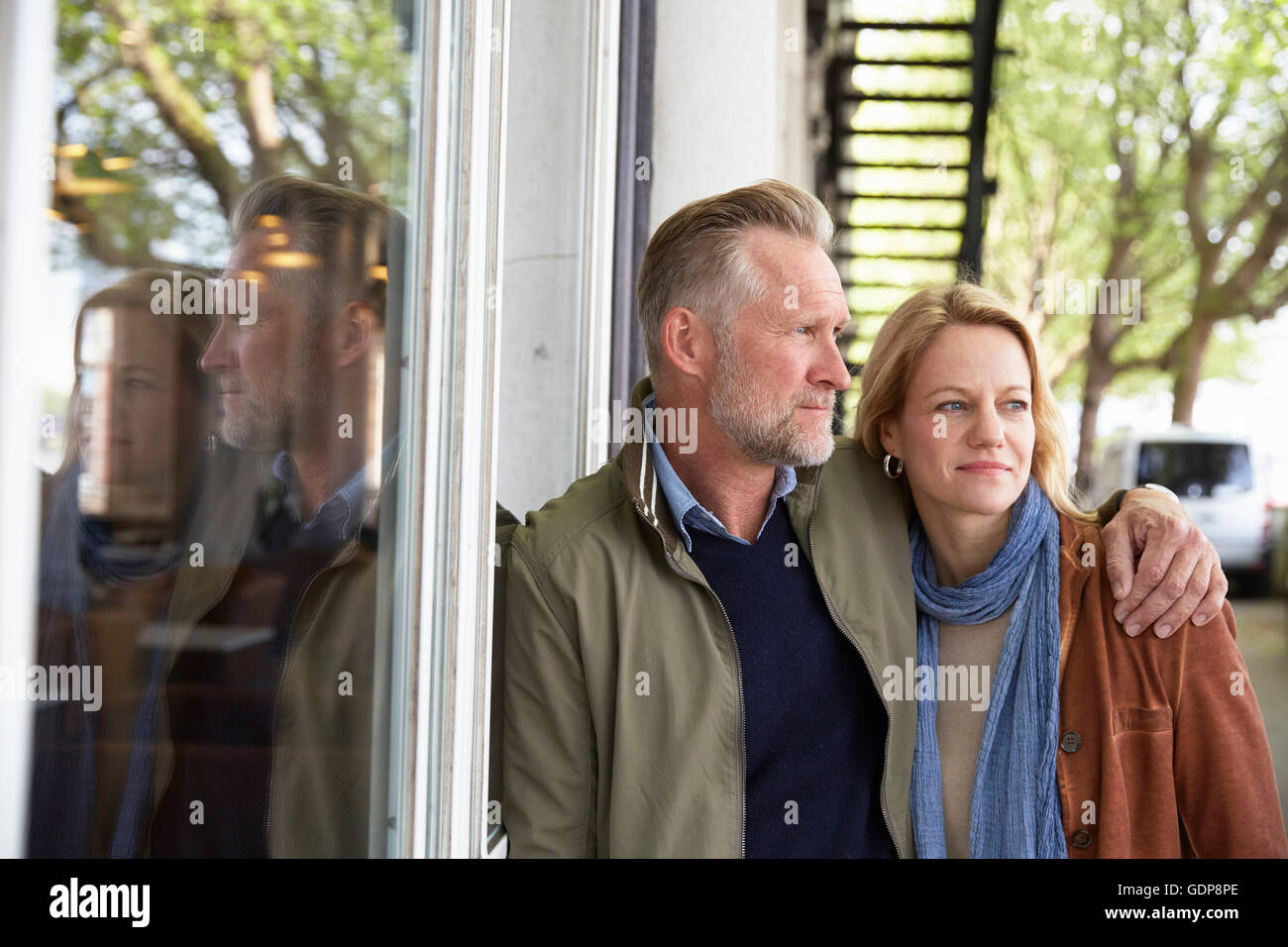 Mature couple leaning against window looking away Banque D'Images