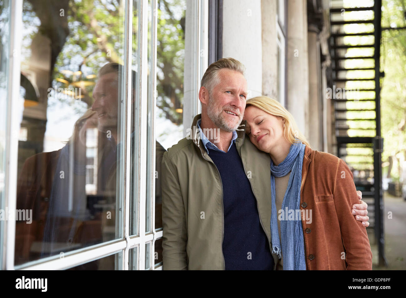 Mature couple leaning against window smiling Banque D'Images