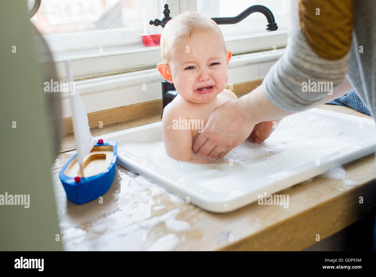 Mère dépose bébé contrarié de son évier de cuisine Banque D'Images