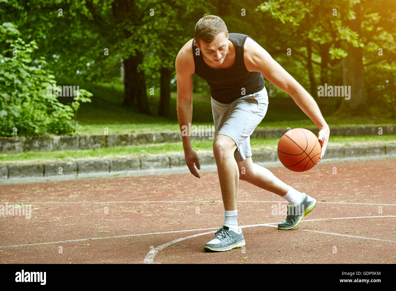 Jeune joueur de basket-ball masculin exécutant avec ball on court Banque D'Images
