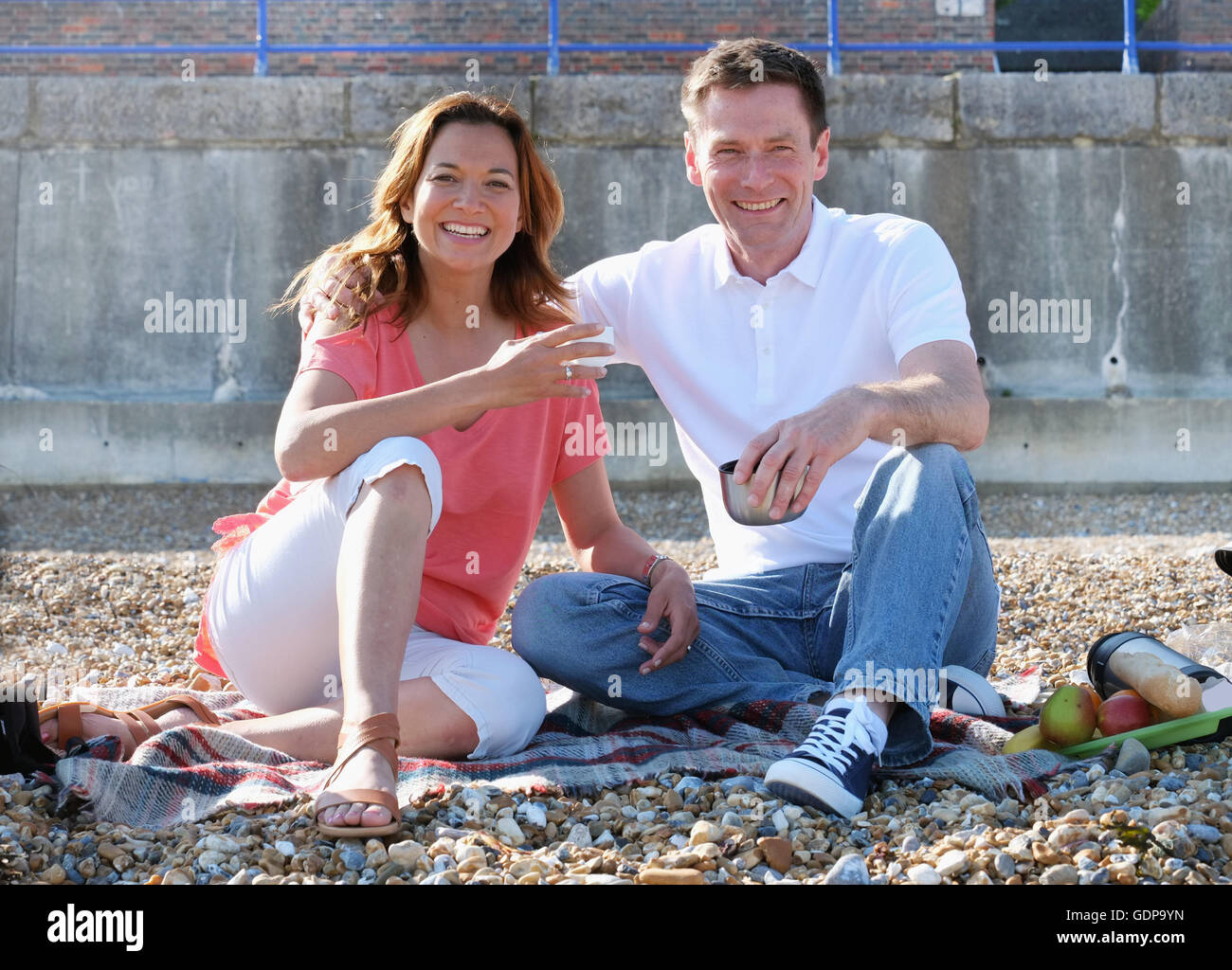 Plage de galets couple having picnic à la caméra en souriant Banque D'Images Plage de galets couple having picnic à la caméra en souriant Banque D'Images