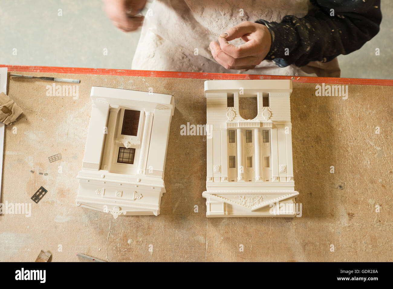 Passage de deux bâtiments modèle à l'échelle de plâtre et de leurs pièces sur une table en bois avec une personne assise à côté d'eux. Banque D'Images