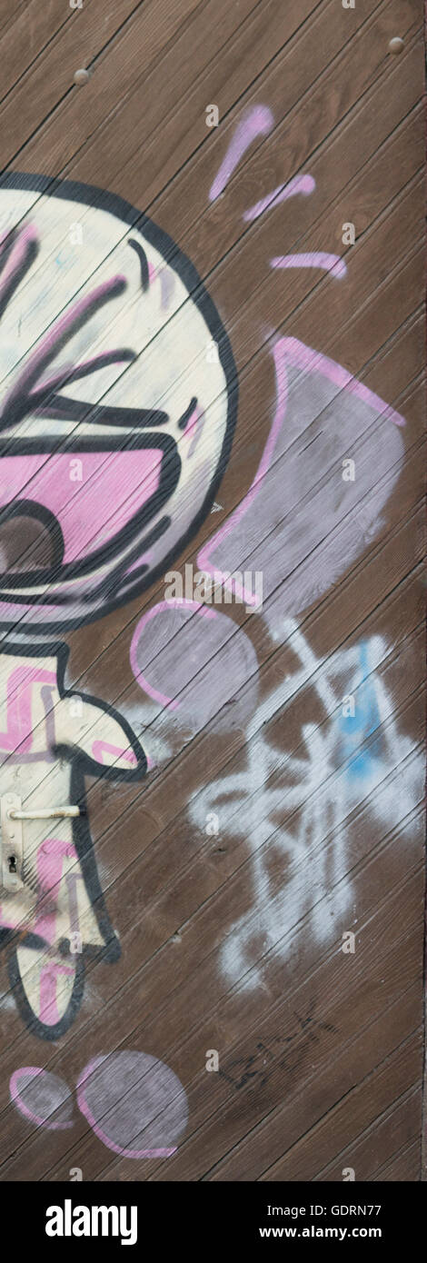 Un puissant art graffiti simple, connu sous le nom de 'Bambin', qui est pulvérisé sur une paroi revêtue, et une grande porte en bois. Banque D'Images