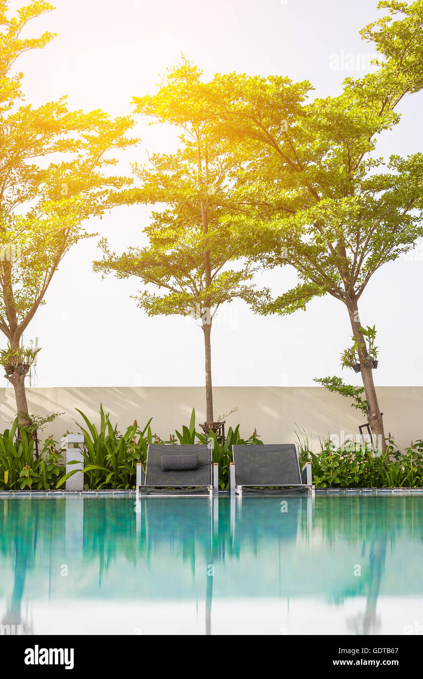 L'accent sur le niveau de la surface de l'eau sur deux sièges de plage mise sur le bord de piscine avec lumière du soleil orange douce Banque D'Images