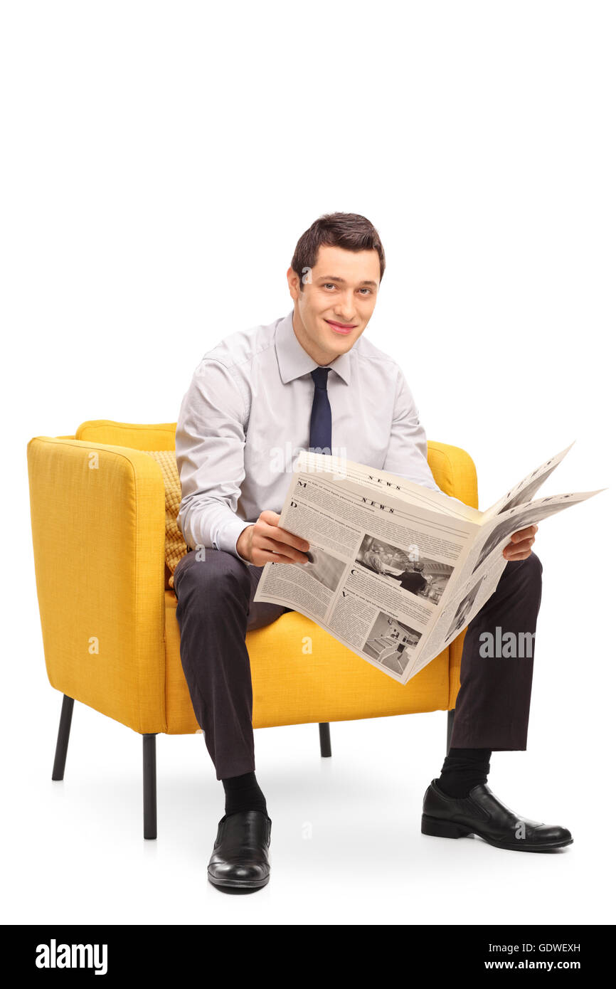 Shot vertical d'un jeune homme d'lire un journal assis sur un fauteuil jaune isolé sur fond blanc Banque D'Images