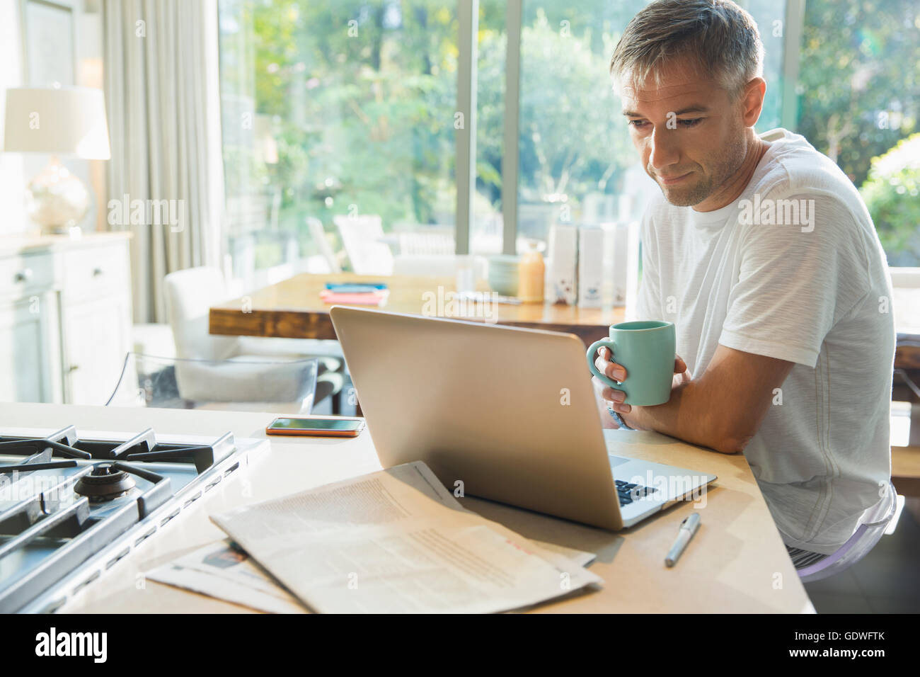 L'homme de boire du café et de travail à l'ordinateur portable dans la cuisine Banque D'Images