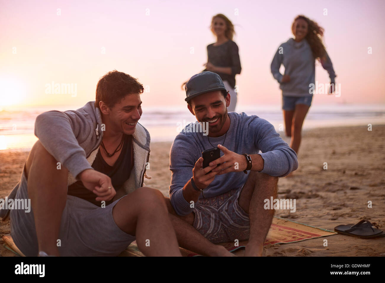 Amis texting with cell phone sur sunset beach Banque D'Images