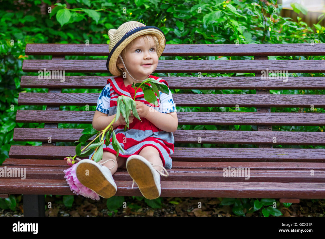 Beau Bébé fille assise sur un banc tenant une fleur Banque D'Images
