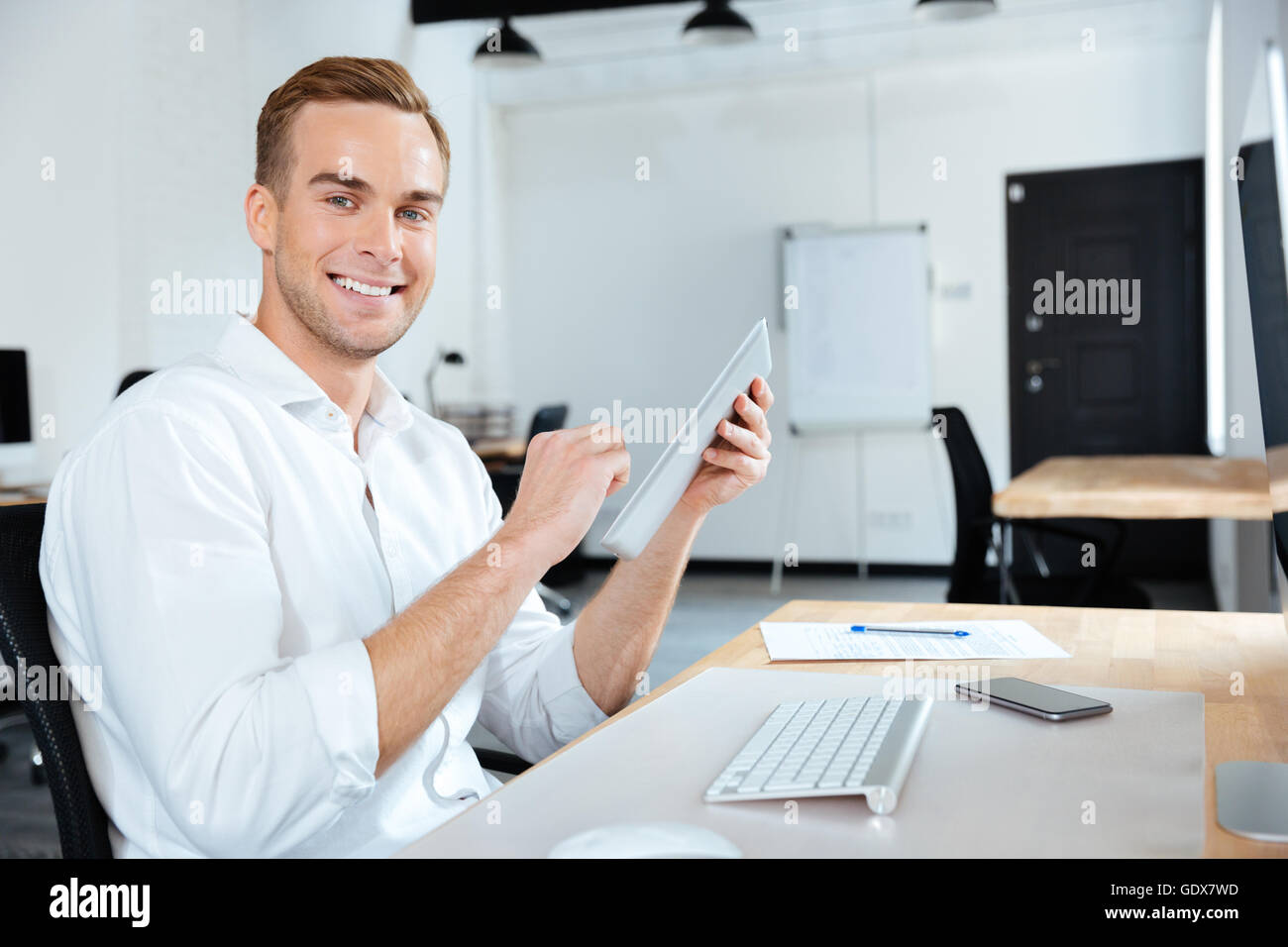 Cheerful young businessman smiling and using tablet à la table Banque D'Images