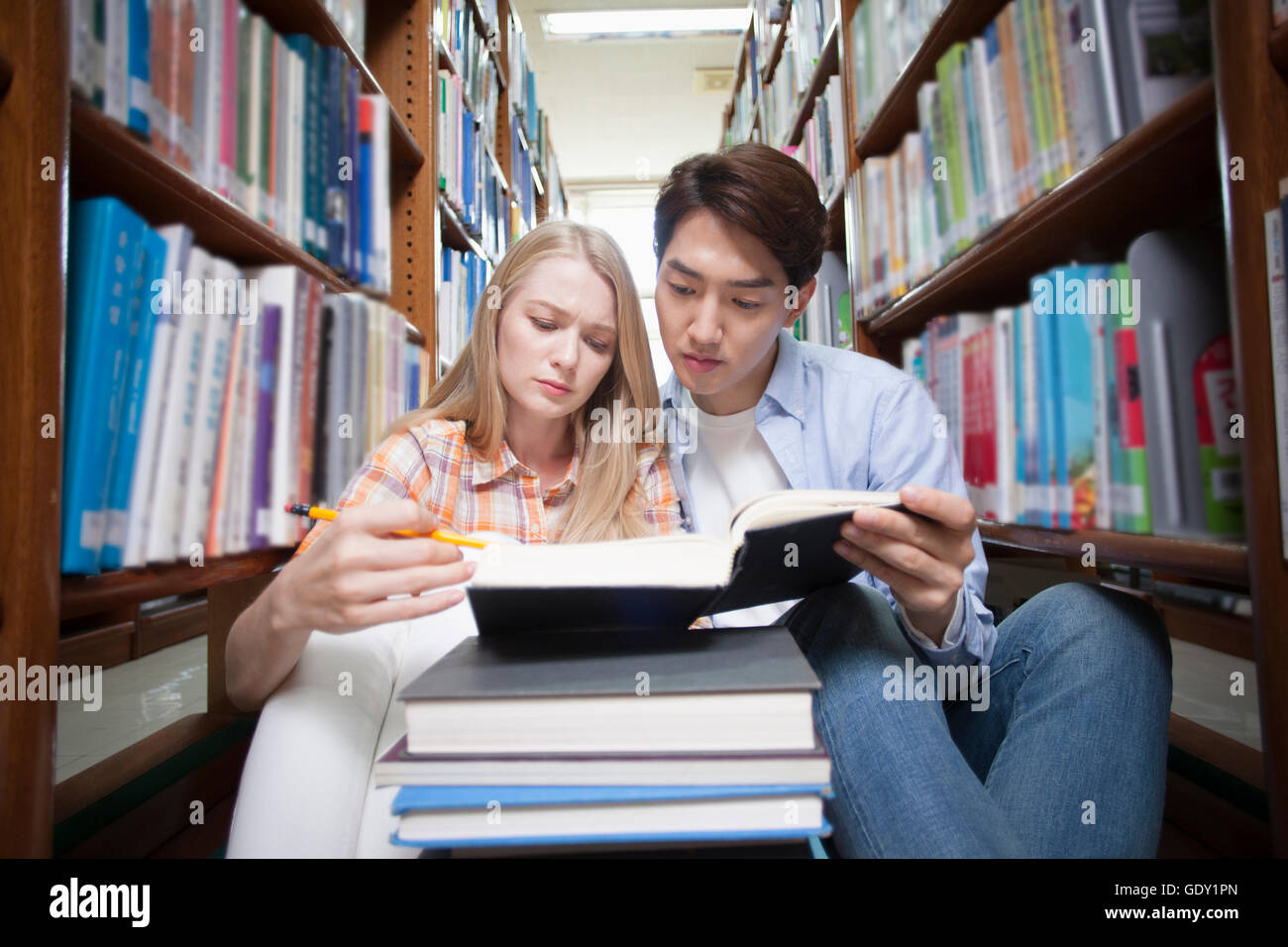 Jeune femme occidentale et orientale jeune homme le partage d'un livre de bibliothèque à la bas Banque D'Images