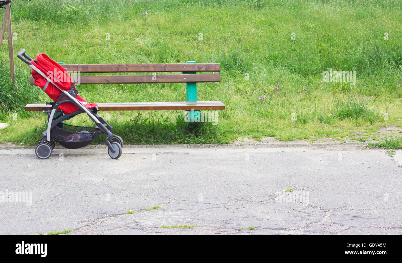 Poussette rouge vide à côté du banc dans le parc Banque D'Images