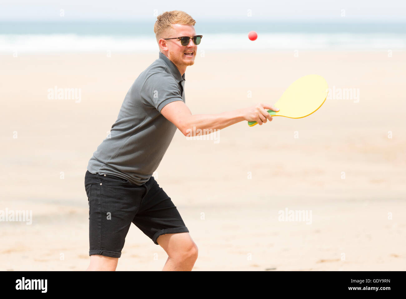 Un jeune homme jouant un jeu de balle et bat sur une plage portant des vêtements casula en été UK Banque D'Images