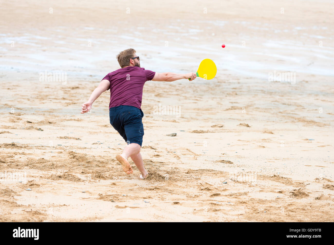 Un jeune homme jouant un jeu de balle et bat sur une plage portant des vêtements casula en été UK Banque D'Images