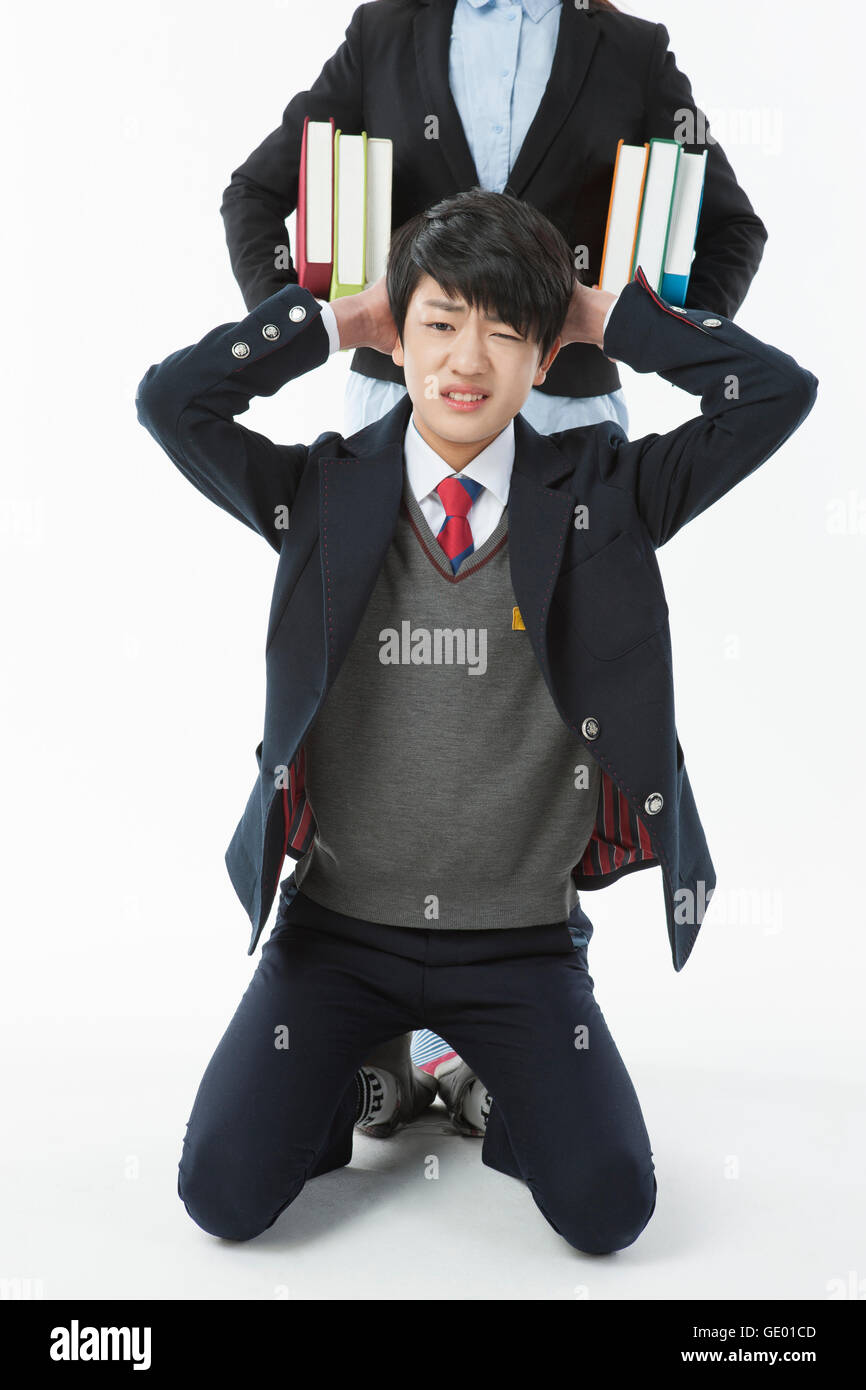 Middle school boy avec un froncement agenouillée fermer ses oreilles avec ses mains et la femme avec des livres derrière lui Banque D'Images