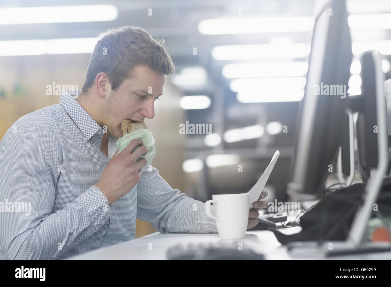 Jeune homme de manger du pain grillé et de la lecture de document Office, Freiburg im Breisgau, Bade-Wurtemberg, Allemagne Banque D'Images