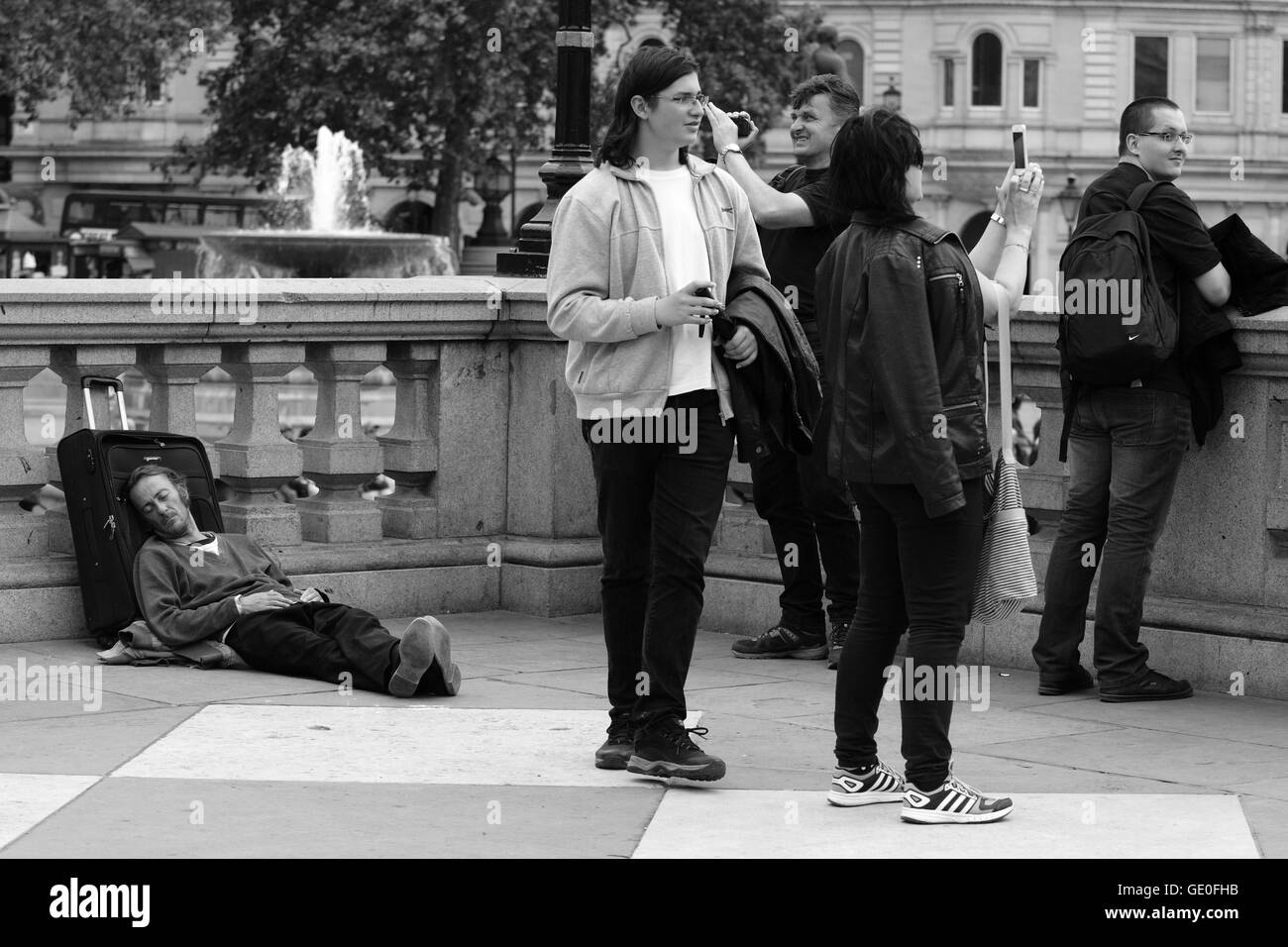 Un estimateur est situé sur le terrain à Trafalgar Square, dormir, tandis que les touristes se trouvent à proximité à la recherche et à la prise de photographies de la Squ Banque D'Images