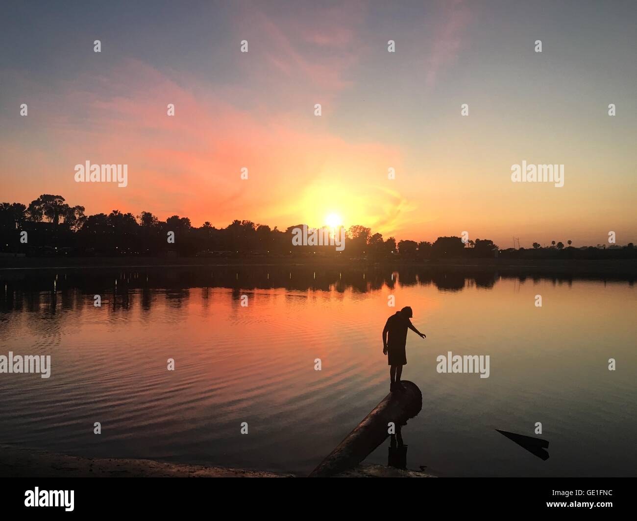 Silhouette d'un garçon debout sur une pipe métallique au bord du lac au coucher du soleil, Orange County, Californie, États-Unis Banque D'Images