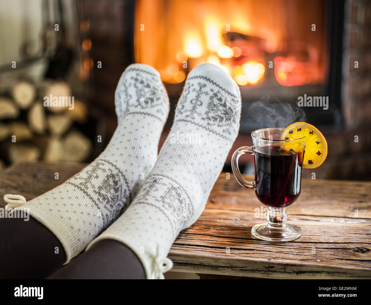 Réchauffement climatique et se reposer près de cheminée. Femme pieds près de la tasse de vin chaud devant le feu. Banque D'Images