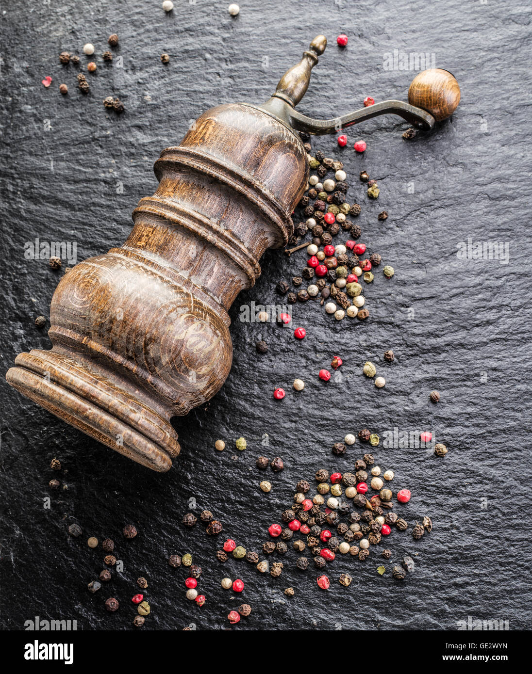 Poivre en grains colorés et vieux moulin à poivre sur le fond noir. Banque D'Images