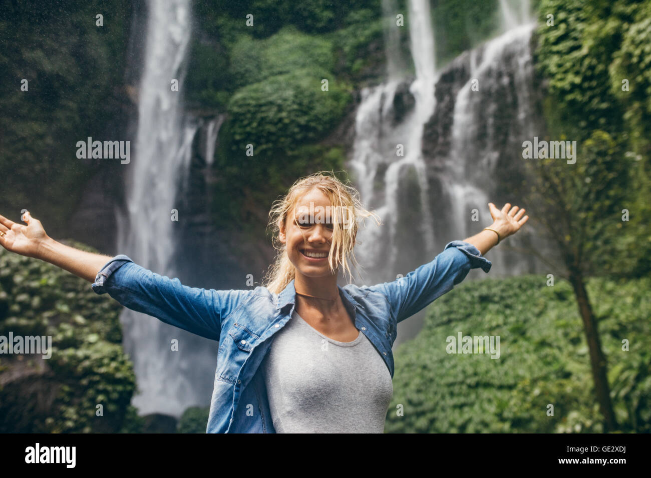 Portrait de jeune femme debout devant une cascade en forêt avec ses mains tendues. Caucasian woman avec tr Banque D'Images