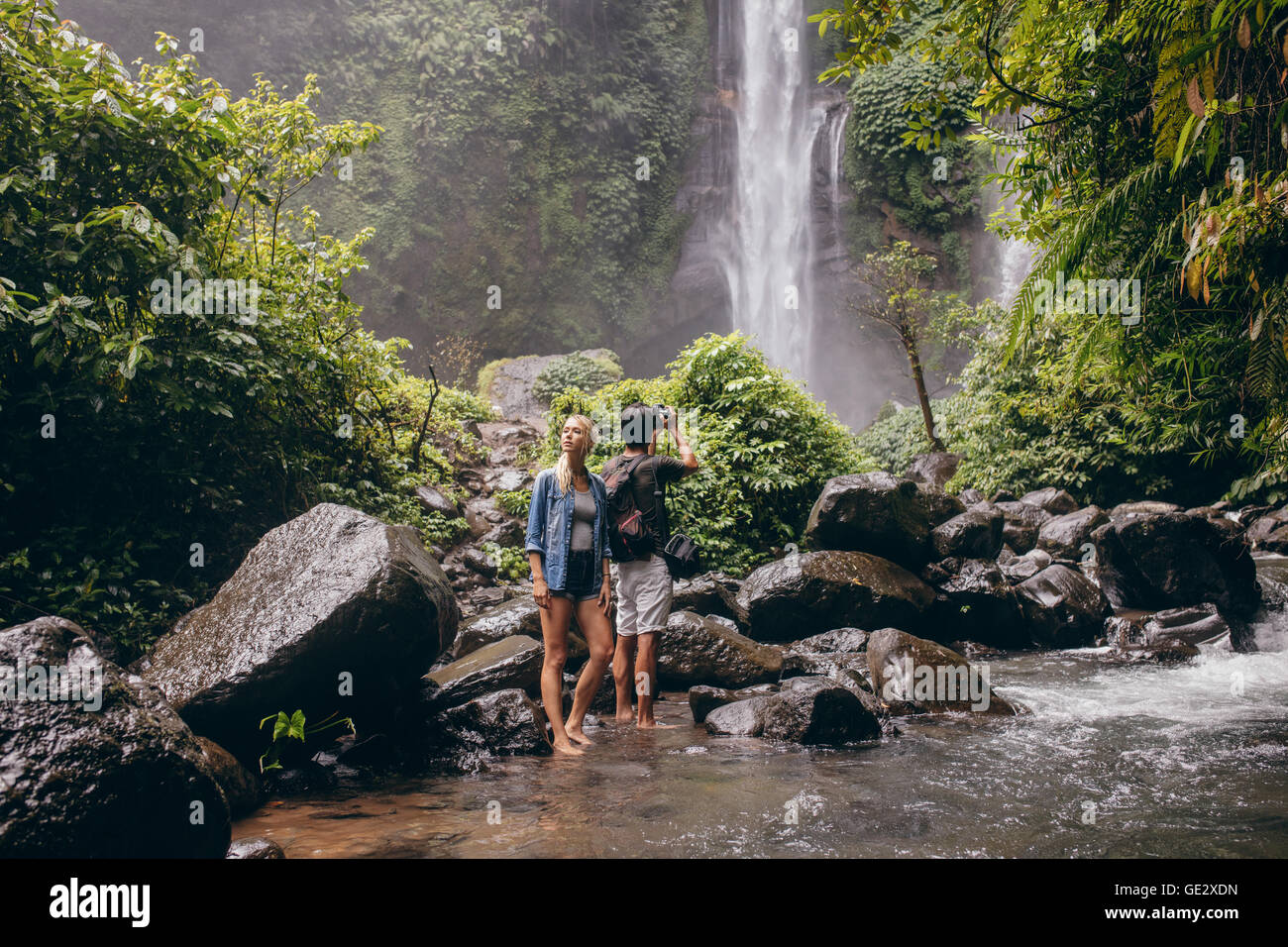 Jeune couple debout près du ruisseau, avec l'homme de prendre des photos de cascade. Couple d'apprécier dans la nature. Banque D'Images