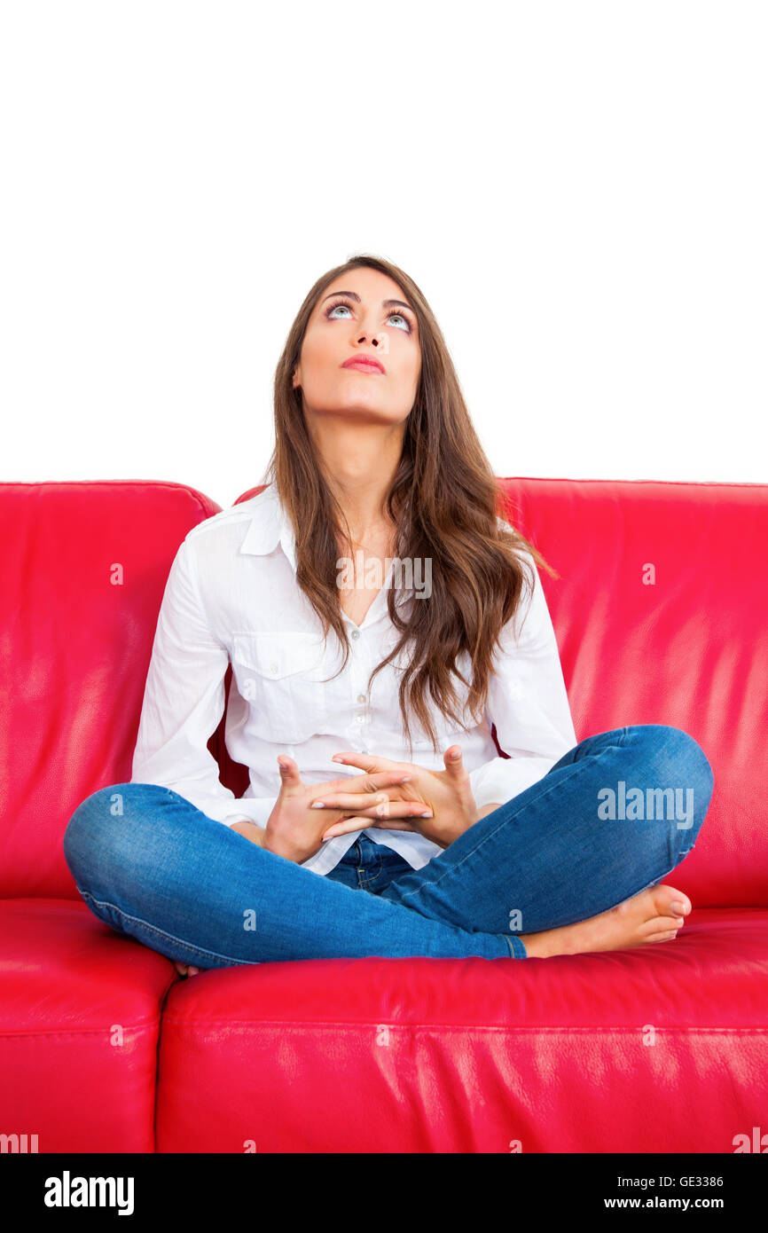 Longueur totale d'une jeune femme. Belle femme avec les mains jointes est assis sur le canapé rouge. Elle est isolée sur fond blanc ba Banque D'Images