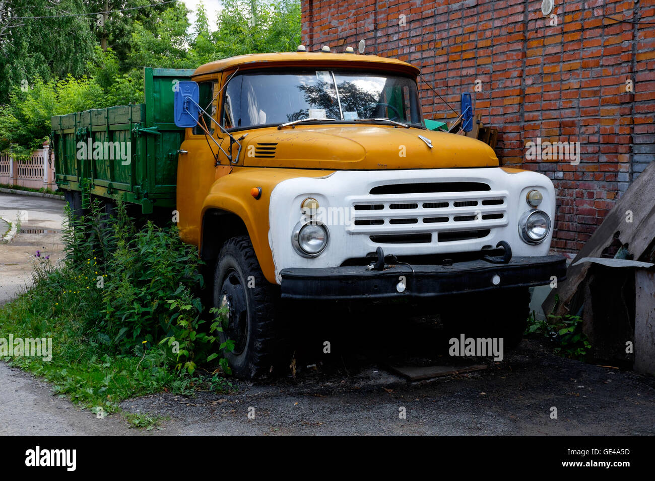 Camion jaune zil couverts par l'herbe verte est stationné près de mur de briques rouges Banque D'Images