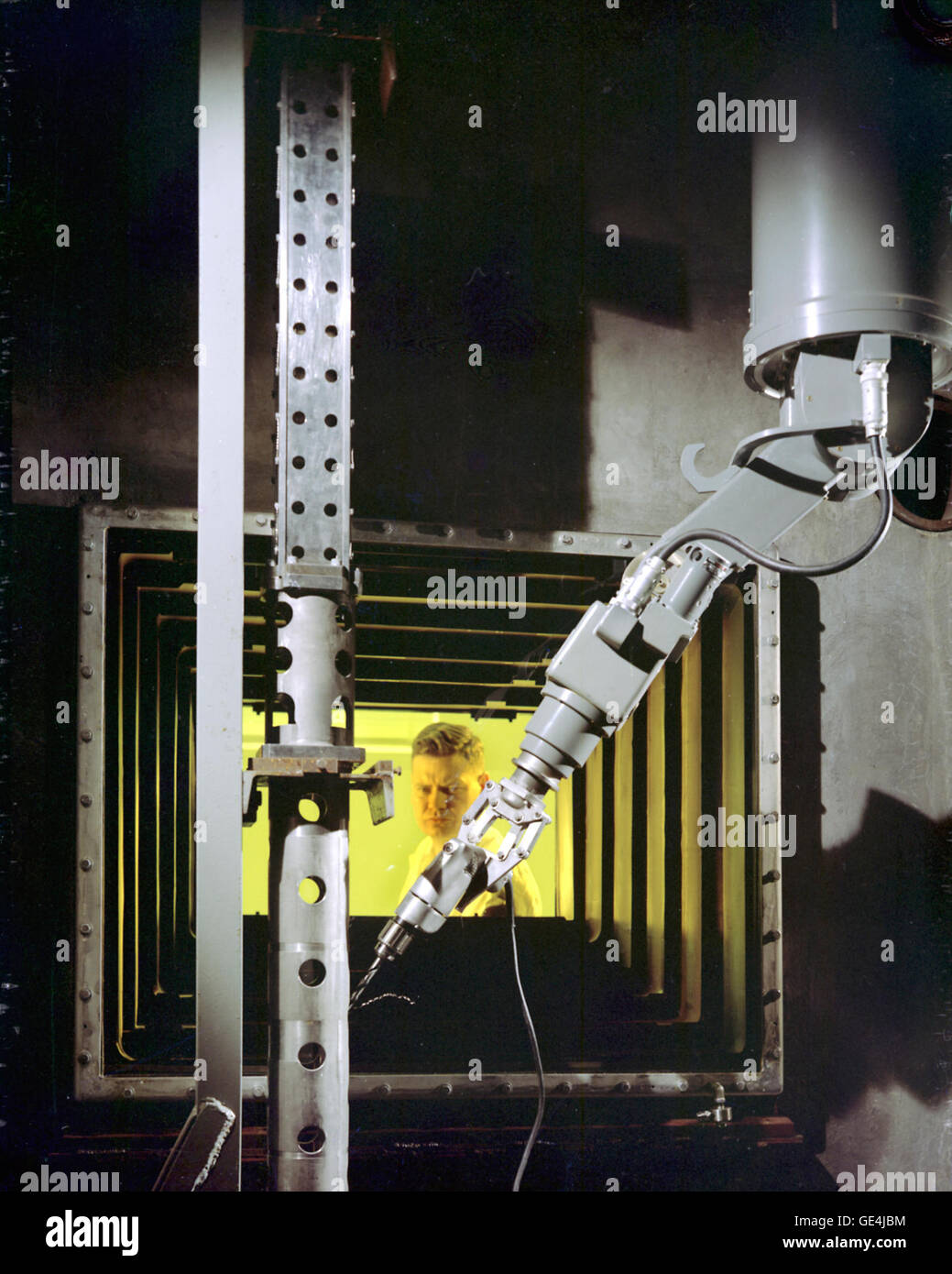Cette photographie montre l’intérieur du laboratoire chaud du réacteur de recherche de Plum Brook. Le bras manipulateur est visible au premier plan, opéré par l'ingénieur Dan Gardner. La fenêtre de protection remplie d'huile élimine la distorsion des rayonnements, garantissant ainsi un fonctionnement sûr dans le laboratoire. Banque D'Images