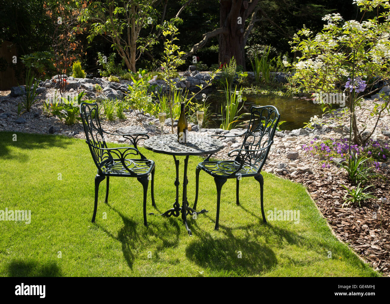 Un jardin en plein soleil, table, chaises, vin, pelouse et étang Banque D'Images