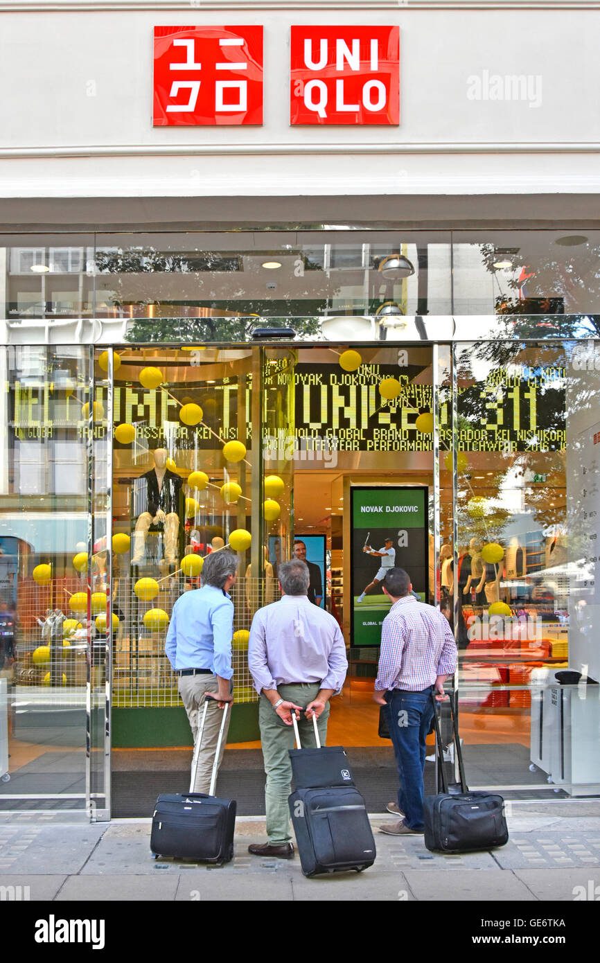 Les hommes de shopping ou de regarder les sports les écrans ? Trois hommes avec petite valise trolleys en scrutant une entrée en boutique Xq Uni Oxford Street London England UK Banque D'Images