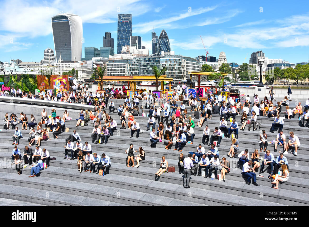 Les employés de bureau de Southwark en prenant un bain à la pause déjeuner ensoleillée More London riverside Scoop amphitheatre avec Ville de toits de Londres au-delà England UK Banque D'Images Les employés de bureau de Southwark en prenant un bain à la pause déjeuner ensoleillée More London riverside Scoop amphitheatre avec Ville de toits de Londres au-delà England UK Banque D'Images