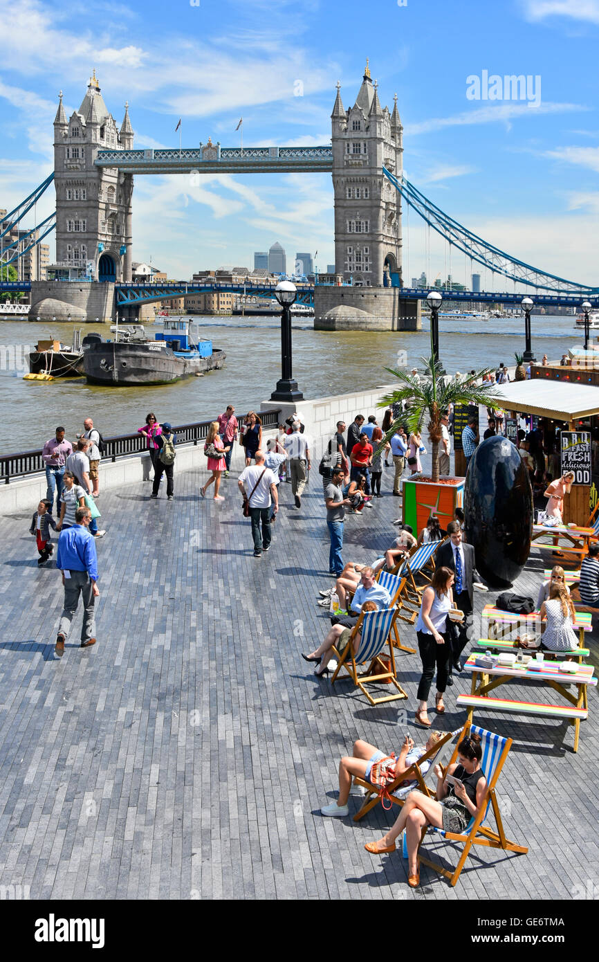 Les touristes et les employés de bureau à l'heure du déjeuner des stands de nourriture rapide mis en place en été, des collations en plein air dans des transats au bord de la Tamise avec le Tower Bridge UK Banque D'Images