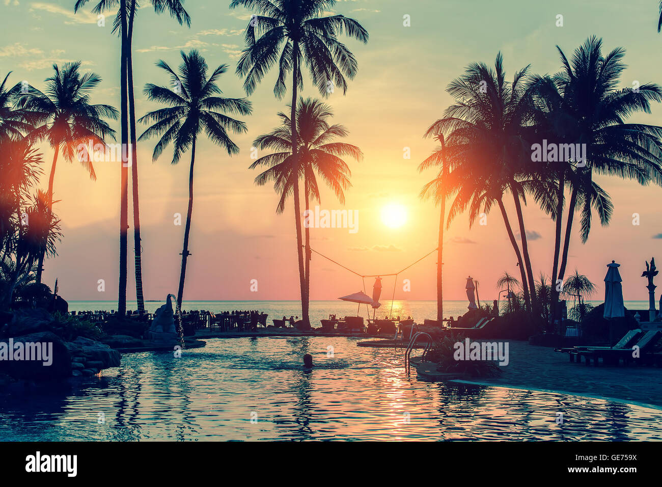 Piscine avec des palmiers près de l'océan lors d'un beau coucher du soleil. Banque D'Images