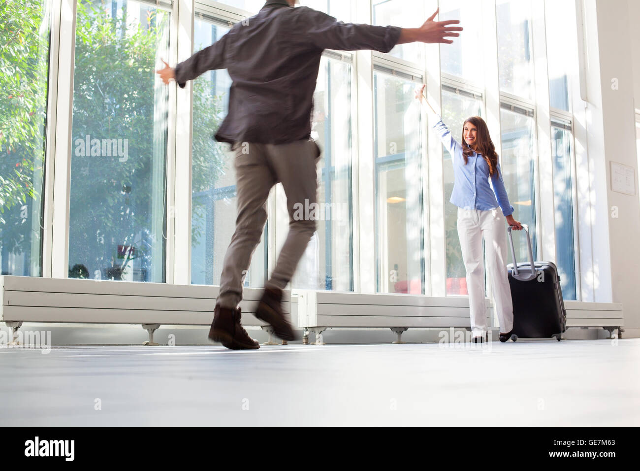 Happy young woman with luggage forme à son petit ami. Homme qui court avec les bras tendus vers la partenaire féminine à l'aéroport. Sh Banque D'Images