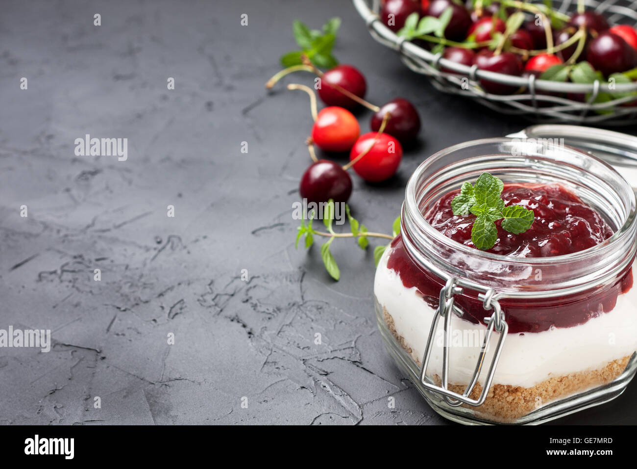 Pas de gâteau au fromage au four dans un bocal en verre avec cerises sur fond noir béton Banque D'Images