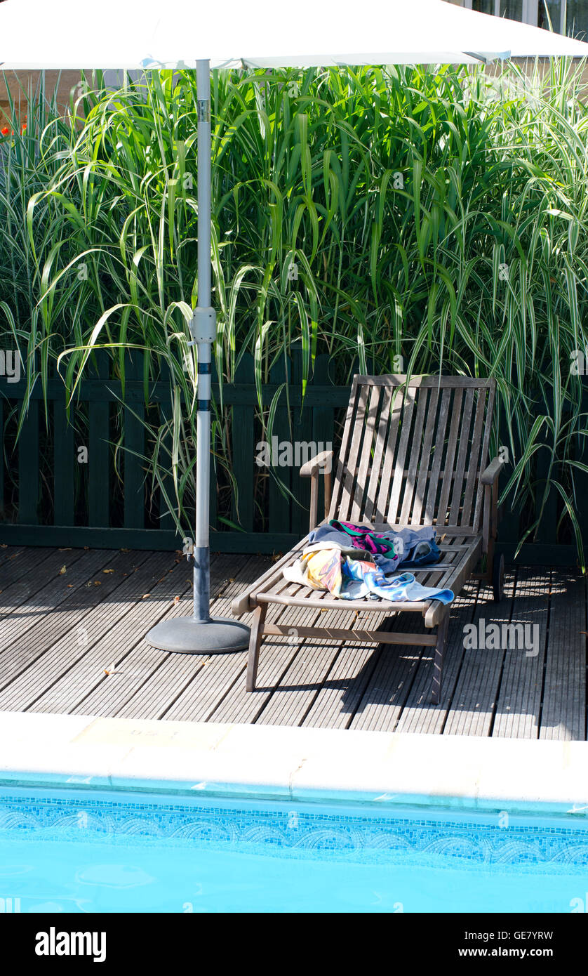 Chaise longue en bois avec piscine par les serviettes et vêtements Banque D'Images