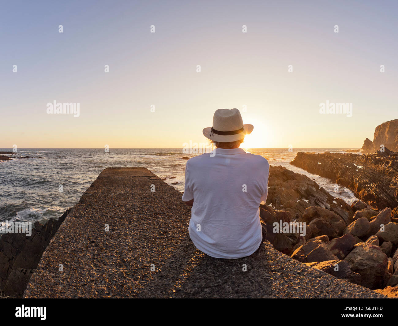 Le Portugal, Senior man sitting on wall at Harbor au coucher du soleil Banque D'Images