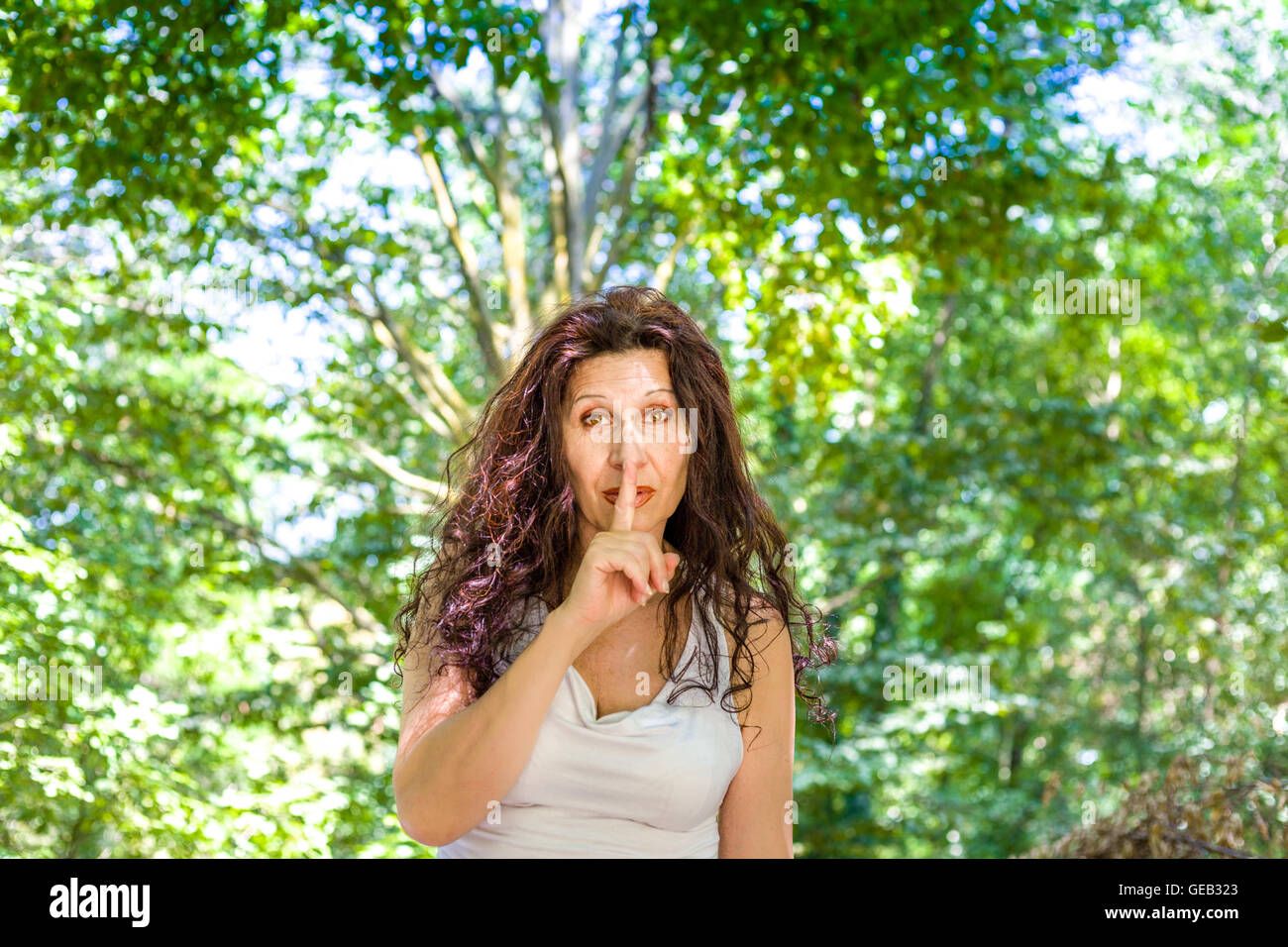 Femme mature chic en courbes, met l'index sur les lèvres pour demander le silence dans un jardin Banque D'Images