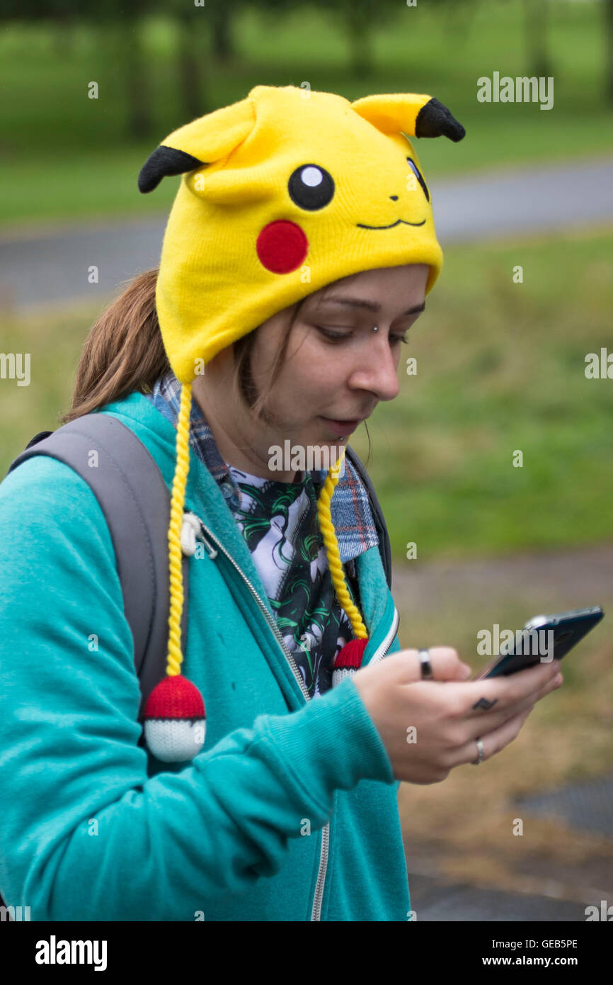 Une jeune fille tient son téléphone portable tout en jouant à Pokemon rendez en portant un Pokemon Pikachu hat. Banque D'Images