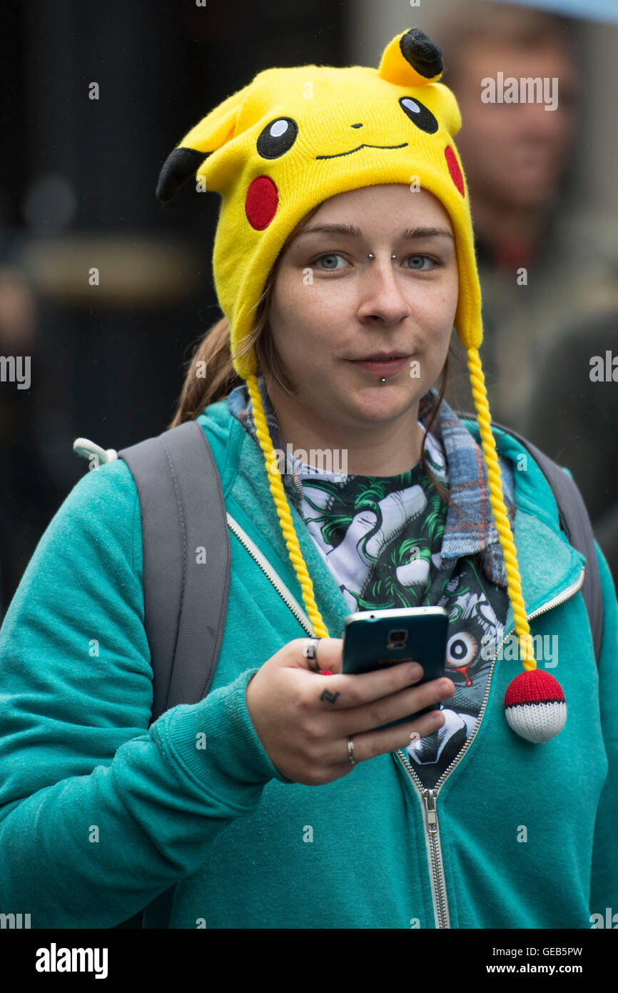 Une jeune fille tient son téléphone portable tout en jouant à Pokemon rendez en portant un Pokemon Pikachu hat. Banque D'Images