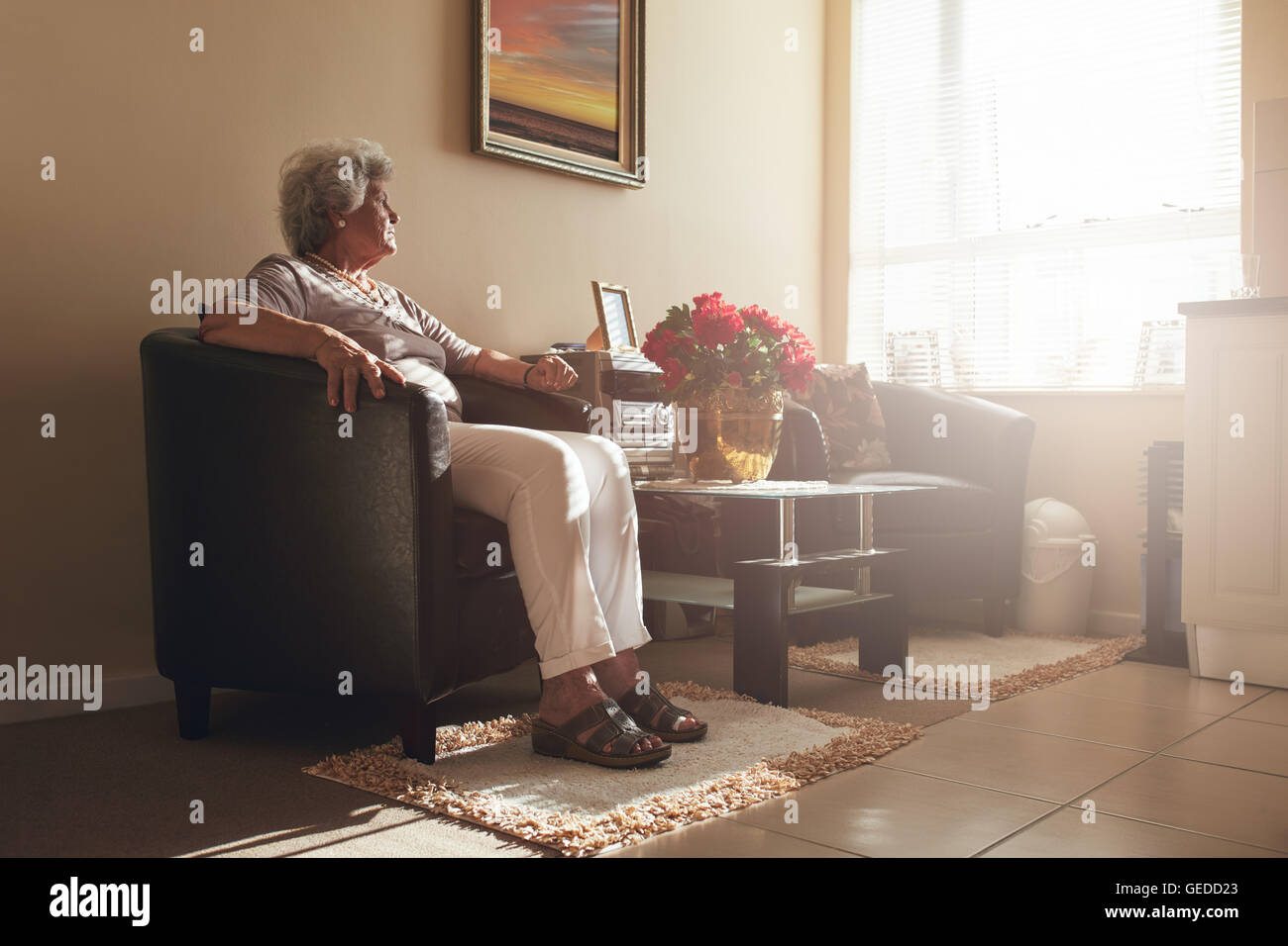 Hauts femme assise seule sur une chaise à la maison. Retired woman relaxing in living room. Banque D'Images