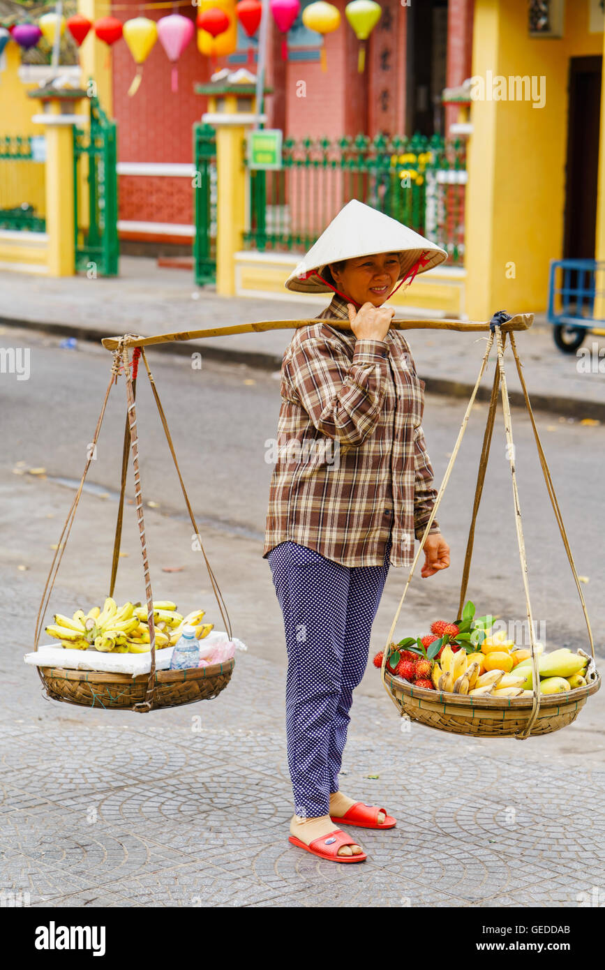 Hoi An, Vietnam - 17 Février 2016 : vendeur transportant des fruits dans des bols sur ses épaules dans la rue à Hoi An, au Vietnam. Ramboutan, mangue et banane. Banque D'Images