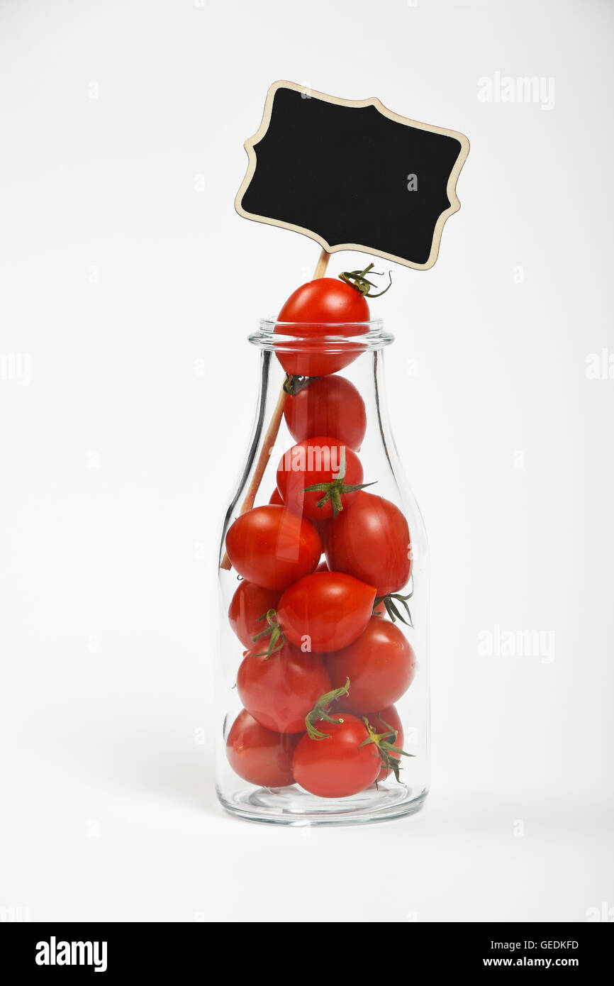 Grande bouteille en verre plein de tomates cerises et tableau noir sur fond blanc comme signe symbole de la matière organique naturelle douce juic Banque D'Images