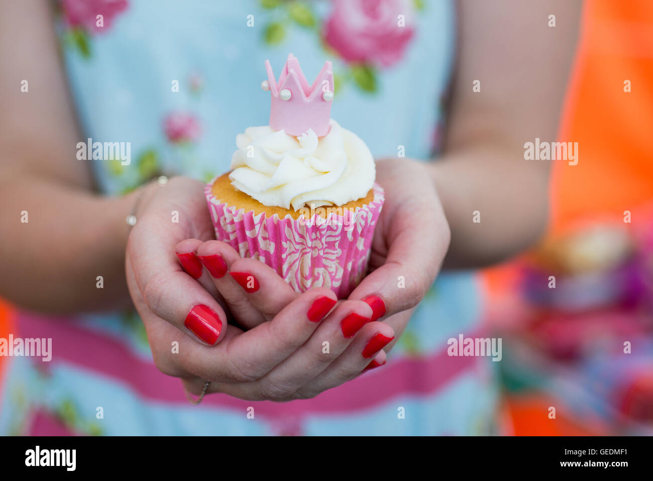 Close up shot of a womans mains tenant un joli cupcake. Elle porte une fleur lumineuse robe la réécriture. Le cupcake est rose et w Banque D'Images