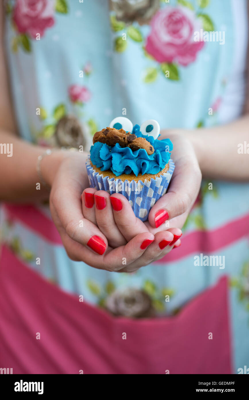Close up shot of a woman's hands holding un joli petit gâteau recouvert de glaçage bleu et un cookie Banque D'Images